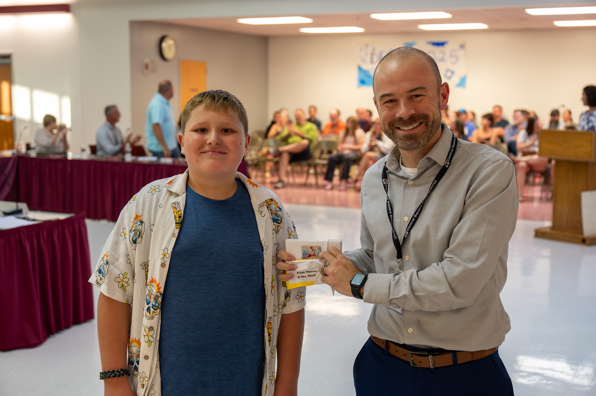 A board of education member standing proudly with a student, who gifted them artwork.